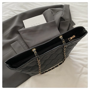 Detail of black quilted tote bag with golden chain strap on a professional backdrop