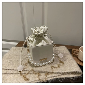 Detail of white bucket bag featuring large pearl handle and gold chain on knit background