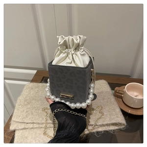 Detail of grey leopard print bucket bag with pearl handle on a wooden table
