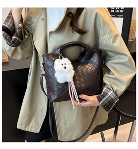 Detail of dark brown woven bucket bag featuring a white plush dog charm and crossbody strap