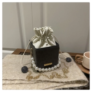 Detail of grey bucket bag featuring a large pearl handle and gold crossbody chain