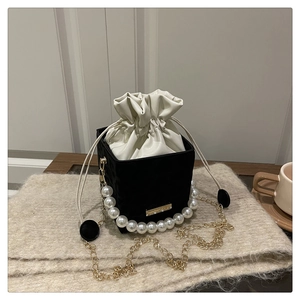 Detail of black and white drawstring bucket bag with pearl handle and gold chain strap