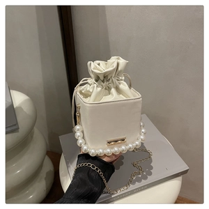 Detail of cream drawstring bucket bag with pearl handle and golden chain strap