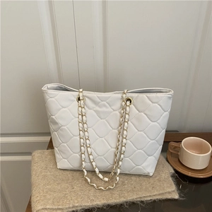 Quilted white tote bag with gold chain strap placed on soft knit for a casual look