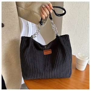 Detail of black corduroy tote bag featuring silver chain strap and leather logo patch