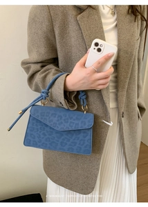Close-up of blue leopard print handbag featuring knotted handle and suede texture