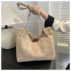 Detail of beige corduroy tote bag with gold chain strap and leather patch logo