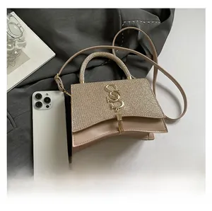 Detail of champagne gold sequin handbag featuring S-shaped metal logo and tassel pendant