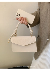 Detail of cream envelope bag featuring knot handle and golden round metal buckle