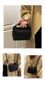 Detail of black leopard print crossbody bag showing handle and shoulder strap usage