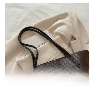 Detail of dark brown faux-crocodile leather tote bag on white blazer with double handles