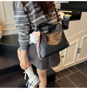 Detail of black woven bucket bag featuring a plush white cat charm on a staircase background