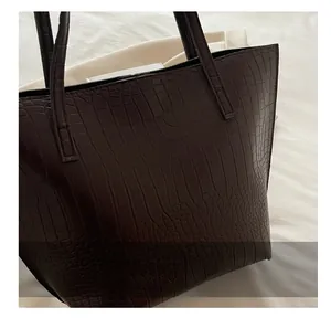Detail of dark brown tote bag featuring luxury crocodile texture and durable leather handles