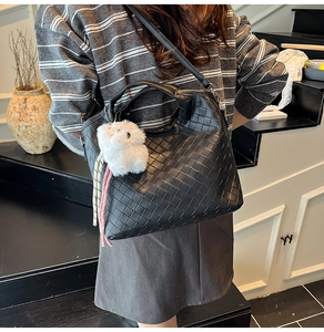 Detail of woven texture black crossbody bag featuring a plush rabbit pendant charm