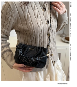 Détail d'un sac bandoulière froncé noir avec chaîne dorée porté par un mannequin