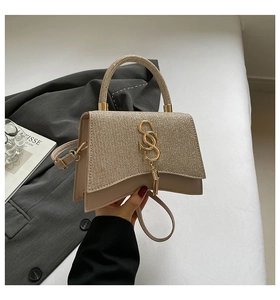 Detail of champagne gold glitter handbag with metallic S logo and elegant tassel fringe