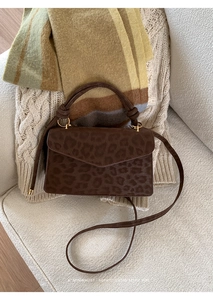 Detail einer dunkelbraunen Handtasche mit Leopardenmuster auf einem cremefarbenen Sofa