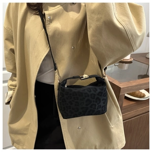 Detail of black leopard pattern handbag with gold clasp worn with a beige trench coat