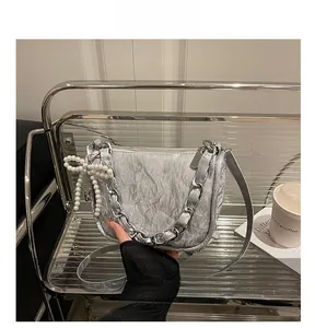 Détail du sac bandoulière argenté plissé avec chaîne épaisse et breloque nœud en perle