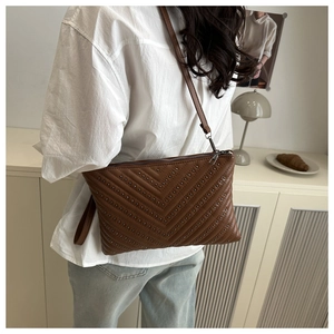 Detail einer dunkelbraunen Stepptasche mit Nieten getragen zu weißer Bluse