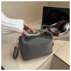 Close-up of a dark grey suede crossbody bag with a golden turn-lock on wooden steps