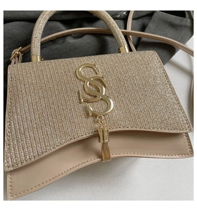 Close-up of champagne glitter texture with gold logo and tassel on the small handbag