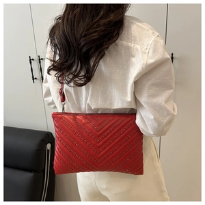Detailansicht einer großen roten gesteppten Clutch mit Nieten, getragen von einem Modell