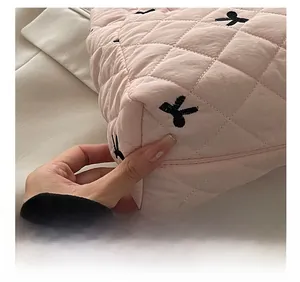 Close-up of pink quilted fabric with black cross embroidery and neat stitching details