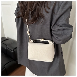 Close-up of cream crossbody bag with leopard embossing and gold clasp worn by a model