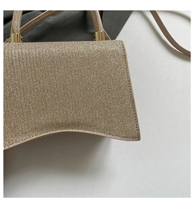 Close-up of golden sequin shoulder bag with curved base and metallic gold strap connectors