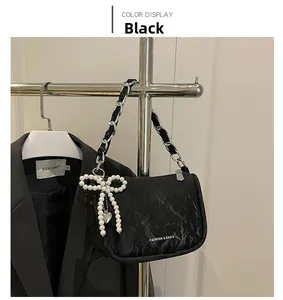 Détail du sac plissé noir avec breloque nœud en perles et bandoulière chaîne