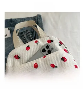 Detail view of strawberry embroidery on white corduroy bag showing front pocket capacity
