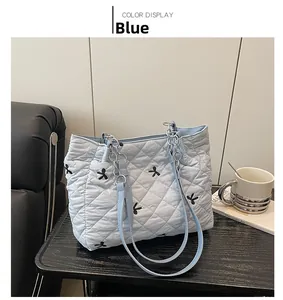 Close-up of light blue quilted tote bag with black bow embroidery and metal chain strap