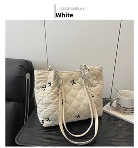 Close-up of white quilted tote bag featuring black bow embroidery and silver chain strap