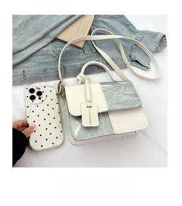Detail of a mini white and silver leather handbag shown next to a smartphone for size scale