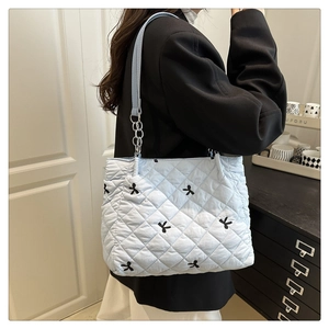 Detail of light blue quilted tote bag with black bow embroidery and metal chain strap