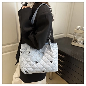 Quilted blue tote bag with black bow patterns shown on shoulder in a lifestyle setting