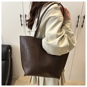 Detail of dark brown tote bag with crocodile pattern worn over the shoulder