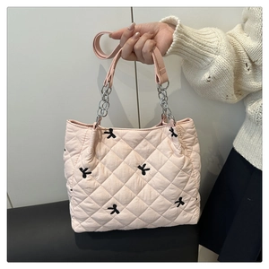 Detail of pink quilted tote bag with black bow embroidery and metal chain strap