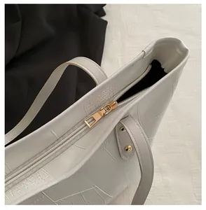 Close-up of golden zipper and croc-embossed texture on a white leather tote bag