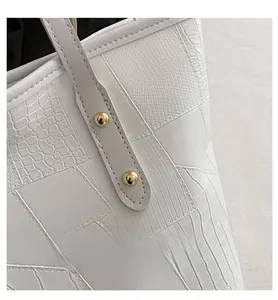 Detail of white crocodile texture leather tote bag with gold round metal rivets