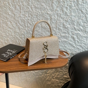 Champagne gold sequin handbag with S-shaped charm and curved base on a wooden table