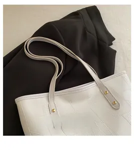 Detail of white crocodile texture tote bag with gold metal rivets on black blazer