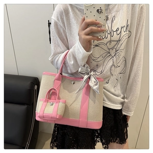 Detail of beige canvas tote with pink leather trim, silk scarf, and mini bag charm