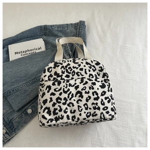 Flat lay of a leopard print corduroy lunch bag next to a book and denim jacket