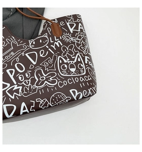 Dettaglio della borsa tote marrone caffè con graffiti di gatti bianchi e manico in pelle