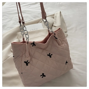 Detail of pink quilted tote bag featuring black bow embroidery and metal chain handles
