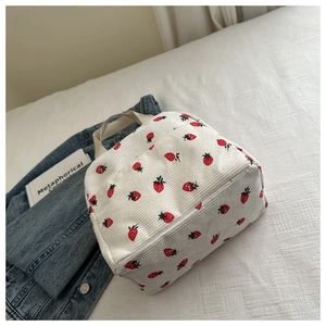 Close-up of white corduroy lunch bag with red strawberry pattern and woven handles