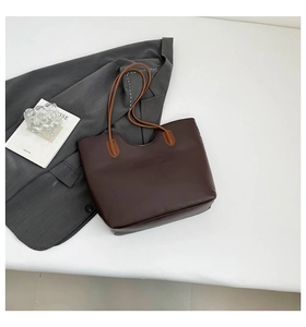 Dettaglio della borsa tote in pelle marrone scuro con spalline sottili su un blazer grigio