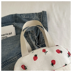 Close-up of white corduroy lunch bag with strawberry print and sturdy ribbon handle